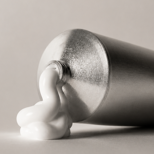 Silver tube of cream with a small amount of cream on a beige background